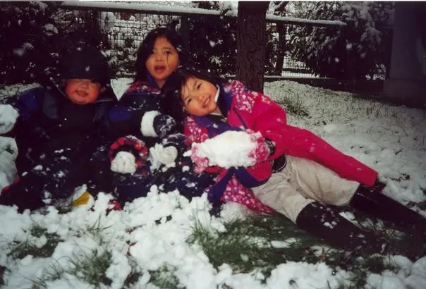 Three kids in winter jackets playing in fresh snow as it falls